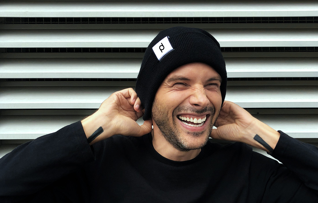 Paul Dersidan smiling in a black beanie in front of striped shutters