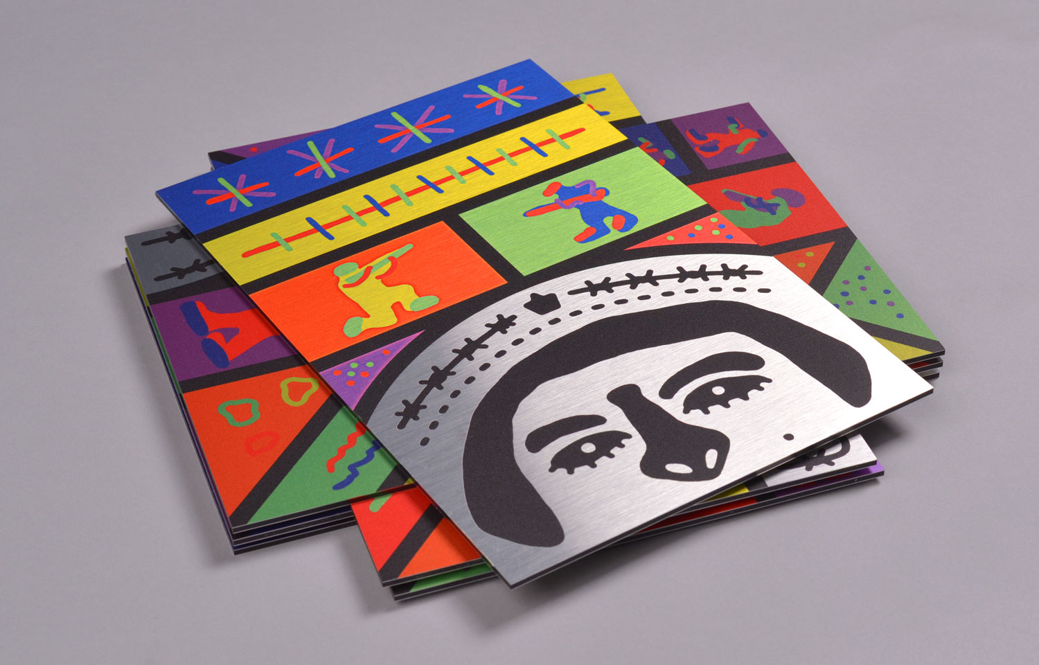 Stack of folded colourful prints featuring a stylised face