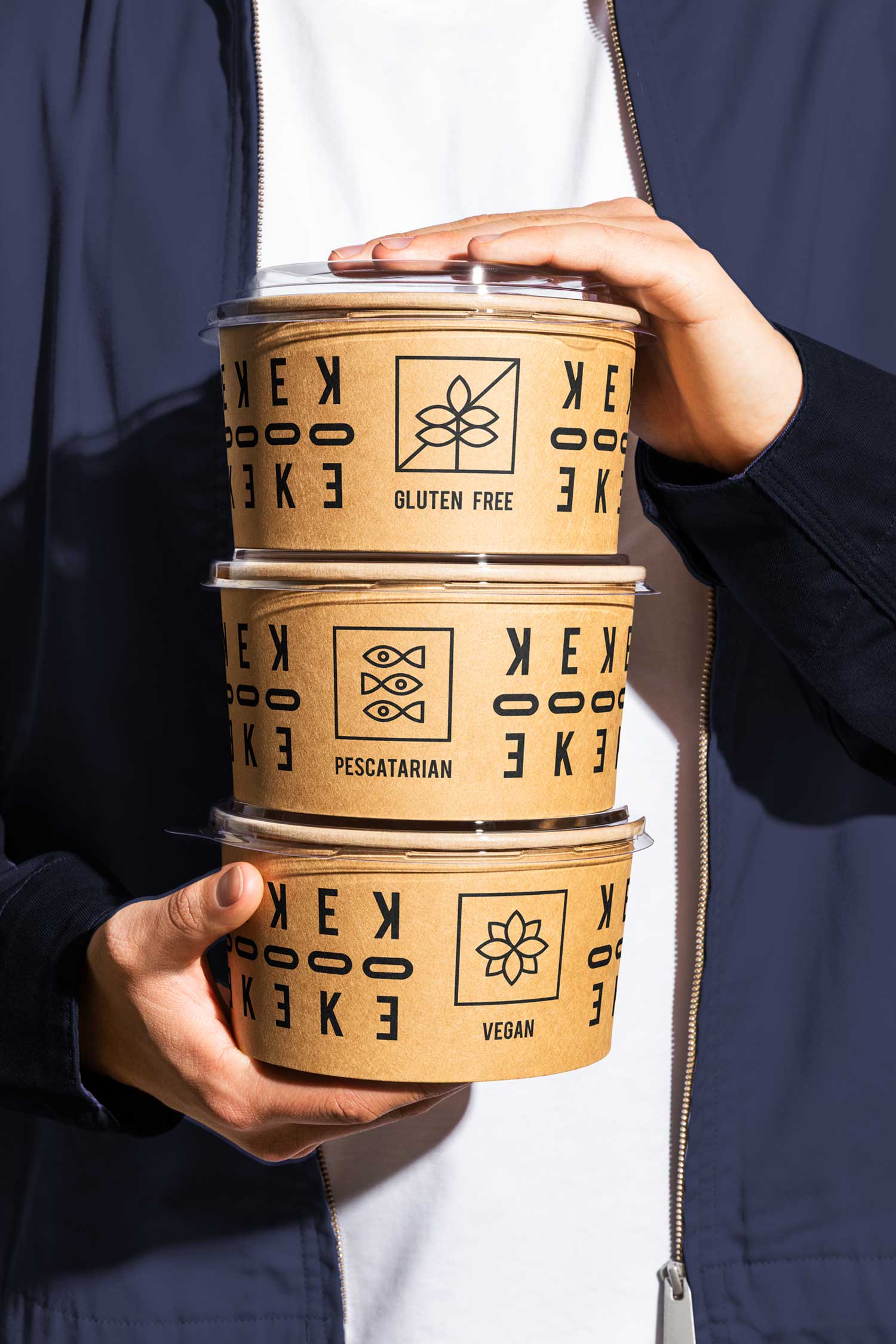 Person holding stacked East of Kitchen food containers marked gluten-free, pescatarian and vegan