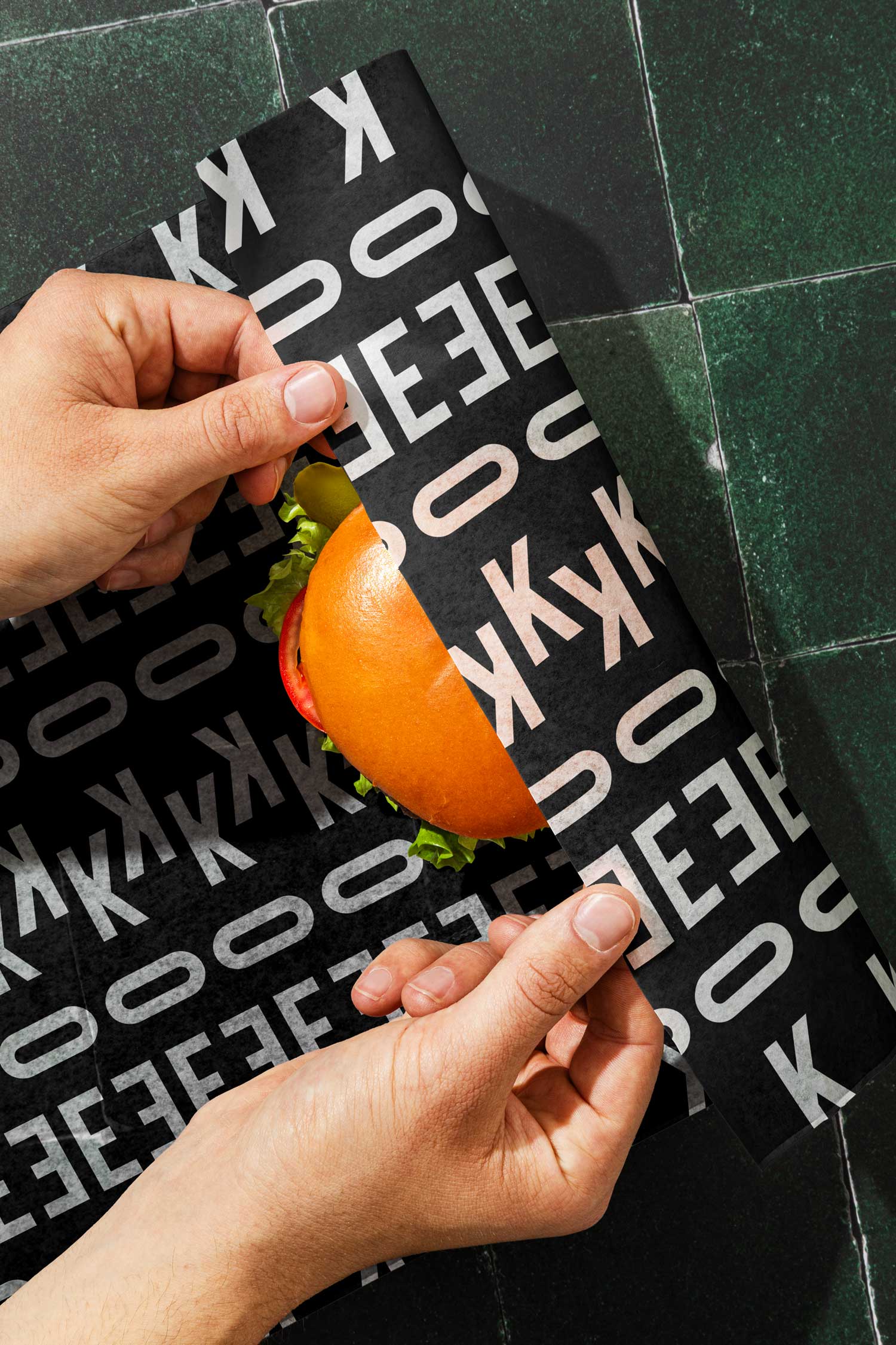 Hands wrapping a burger in black East of Kitchen branded paper