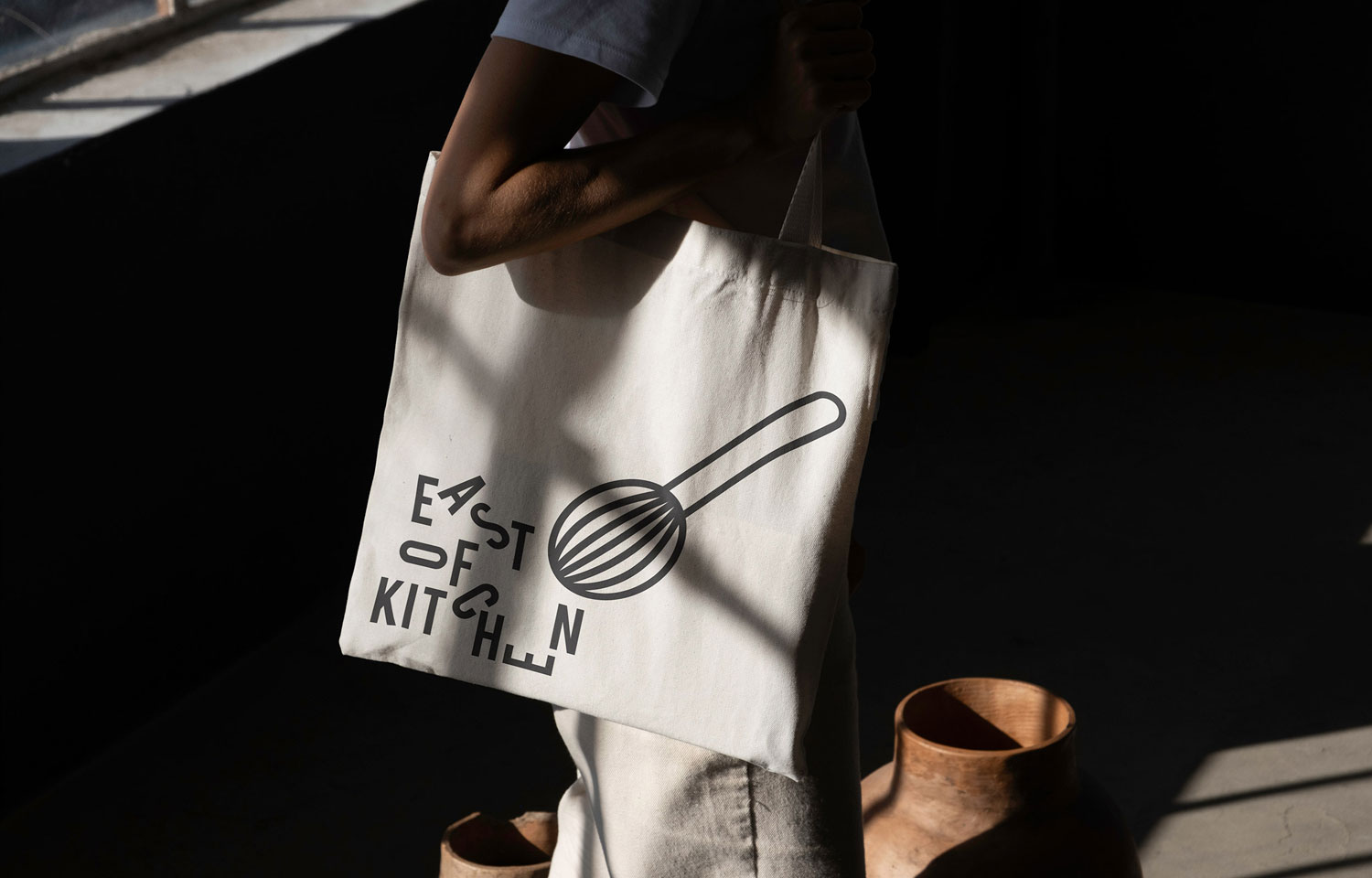 Person holding East of Kitchen tote bag with line drawing