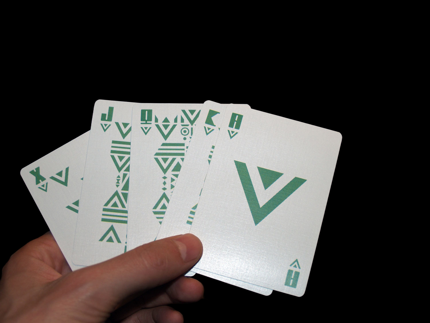 Hand fanning five green geometric playing cards