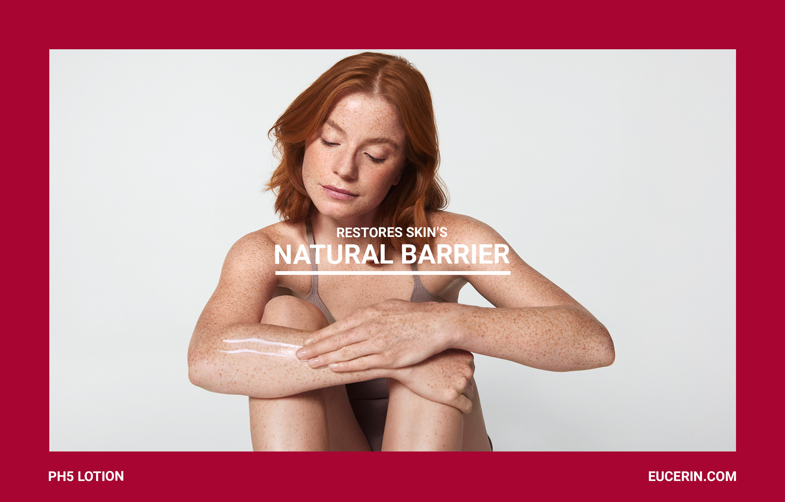 Red-haired woman embracing herself in a burgundy Eucerin Natural Barrier campaign frame
