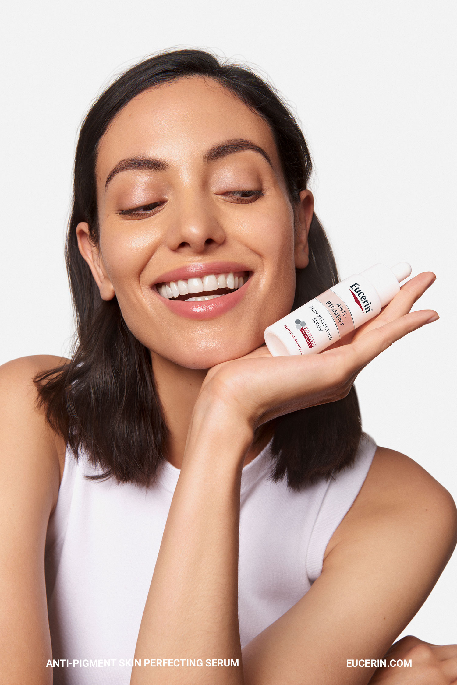 Smiling woman holding a small Eucerin serum bottle under her chin