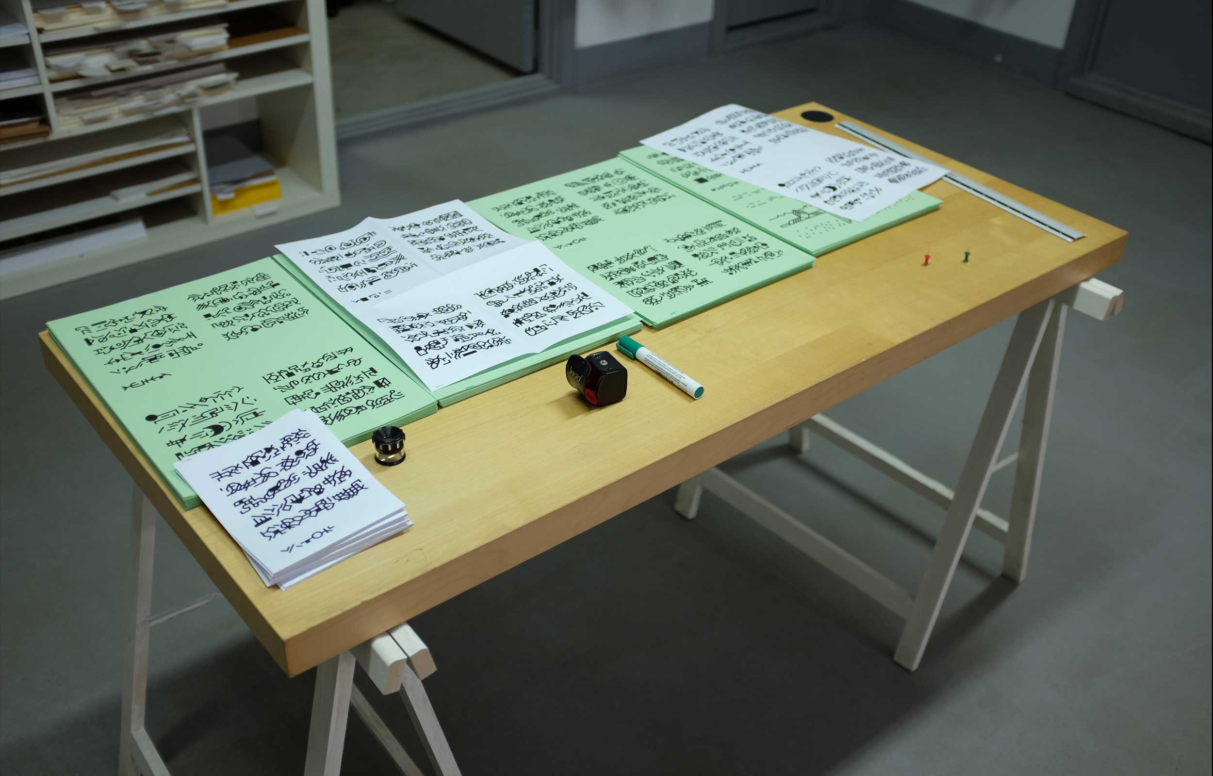 Table laid out with pale green printed sheets and black glyph artwork