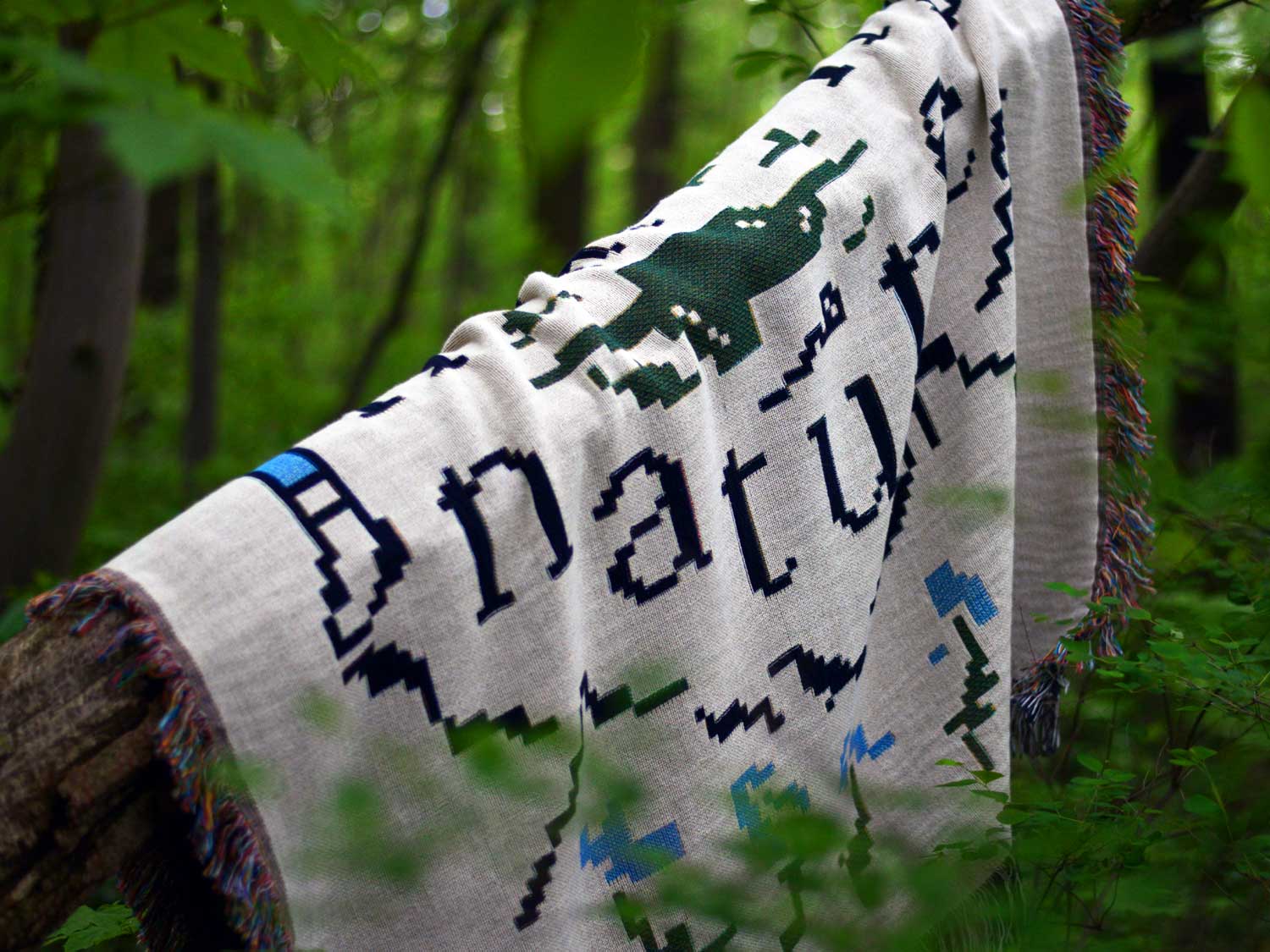 Close-up of a white woven blanket with blue and green Human Nature lettering