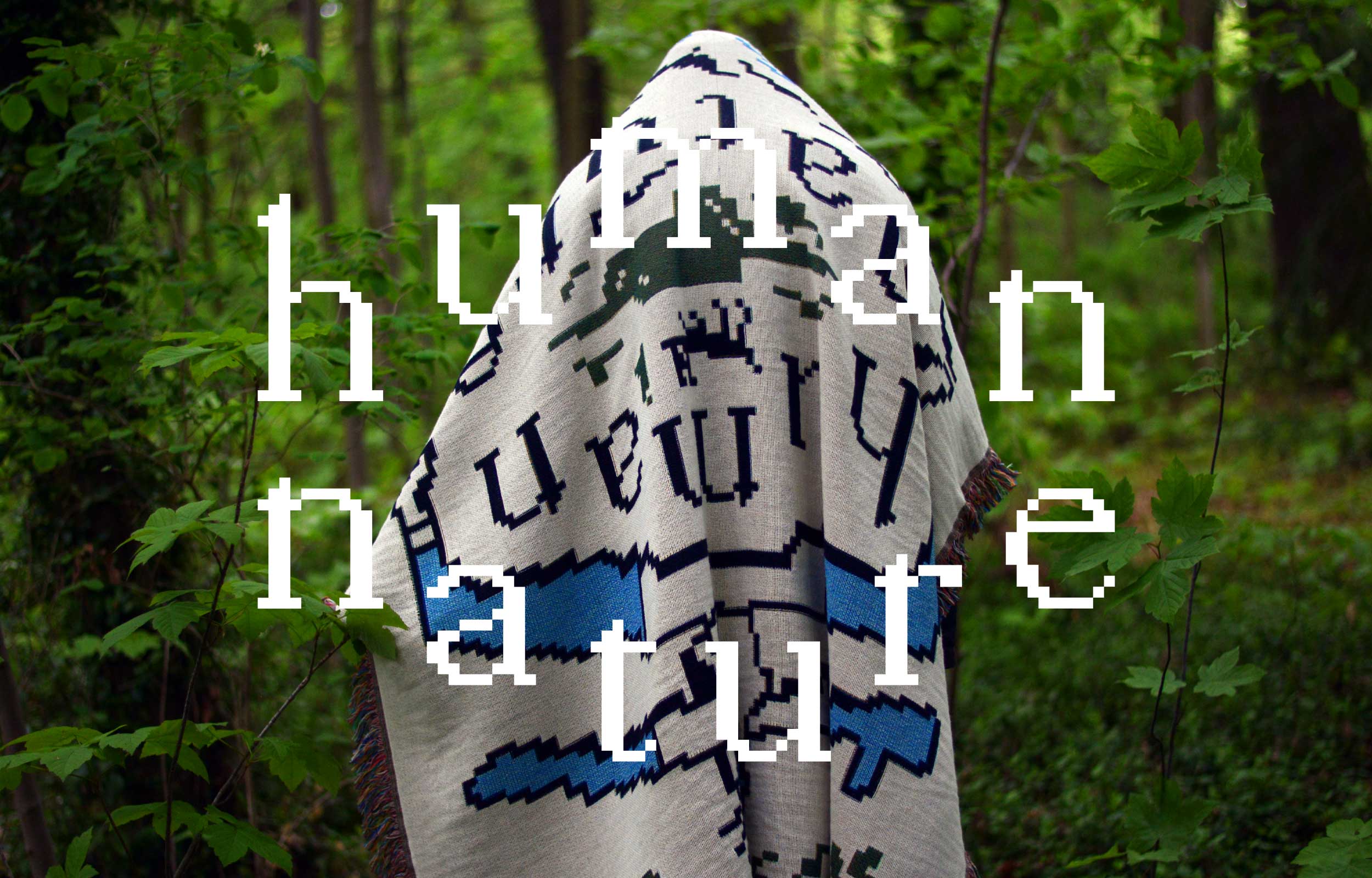 White woven blanket with Human Nature lettering hanging in a green forest
