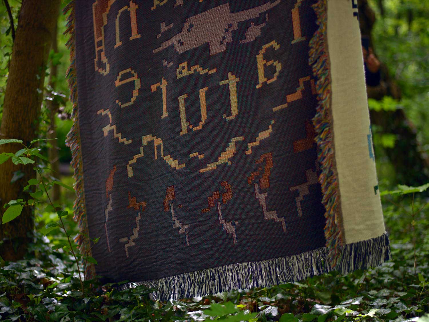 Dark reverse side of a woven blanket with tan geometric lettering in a forest