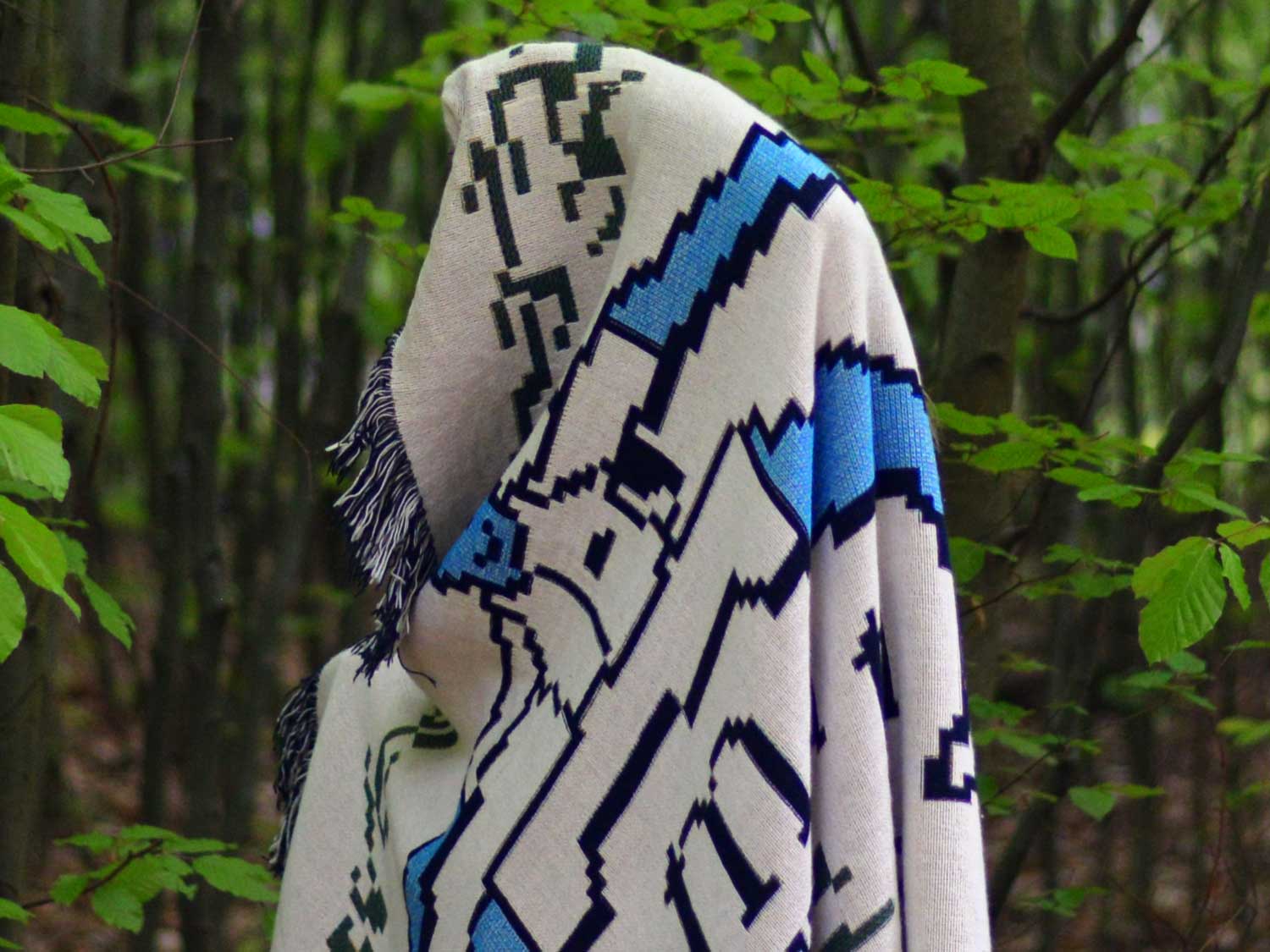 White woven blanket with bold blue geometric lettering draped over a tree