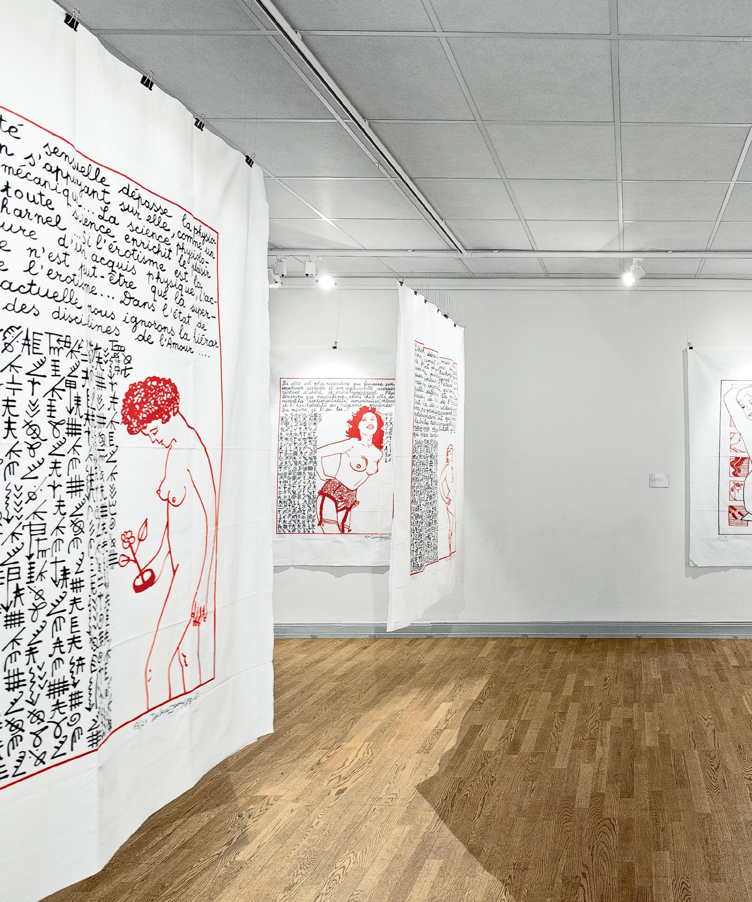 Gallery view with a large hanging text-and-figure artwork and framed works on white walls