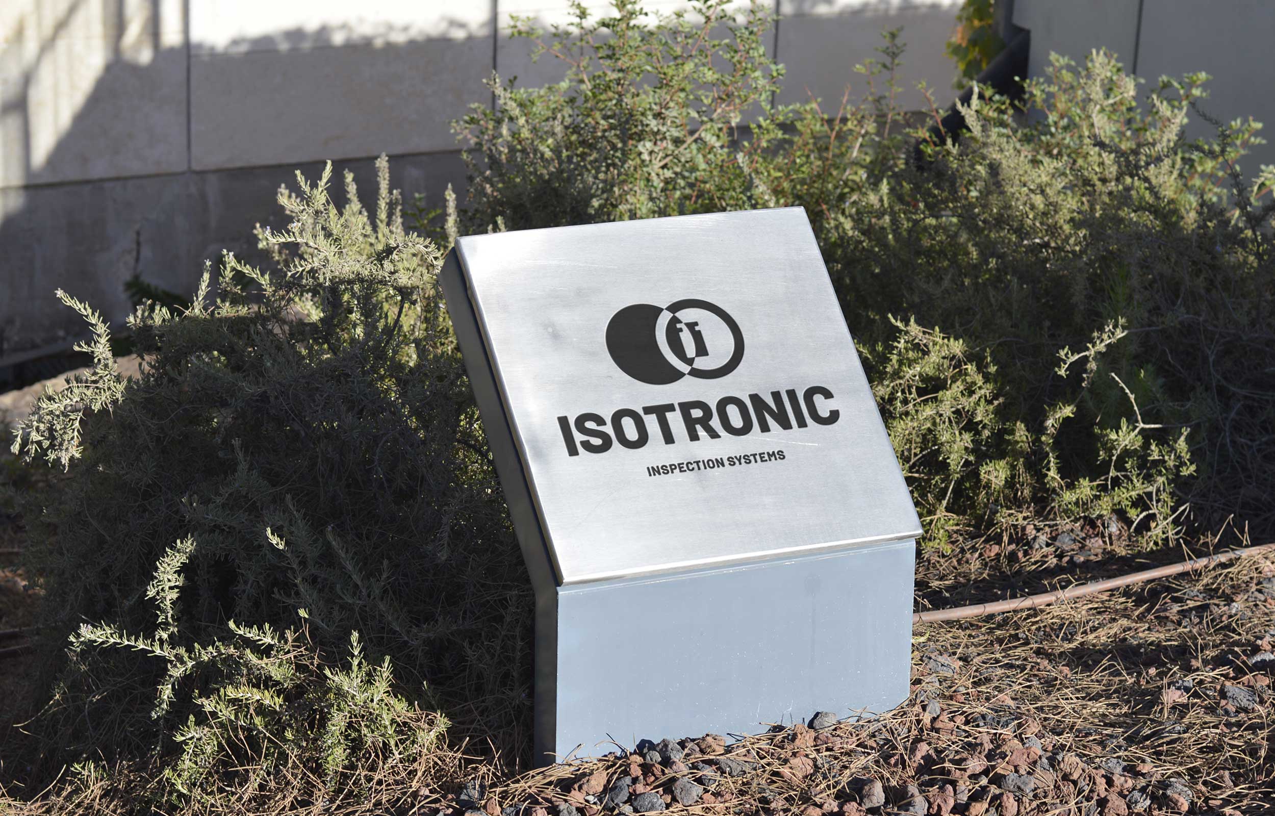 Freestanding white Isotronic sign beside green shrubs