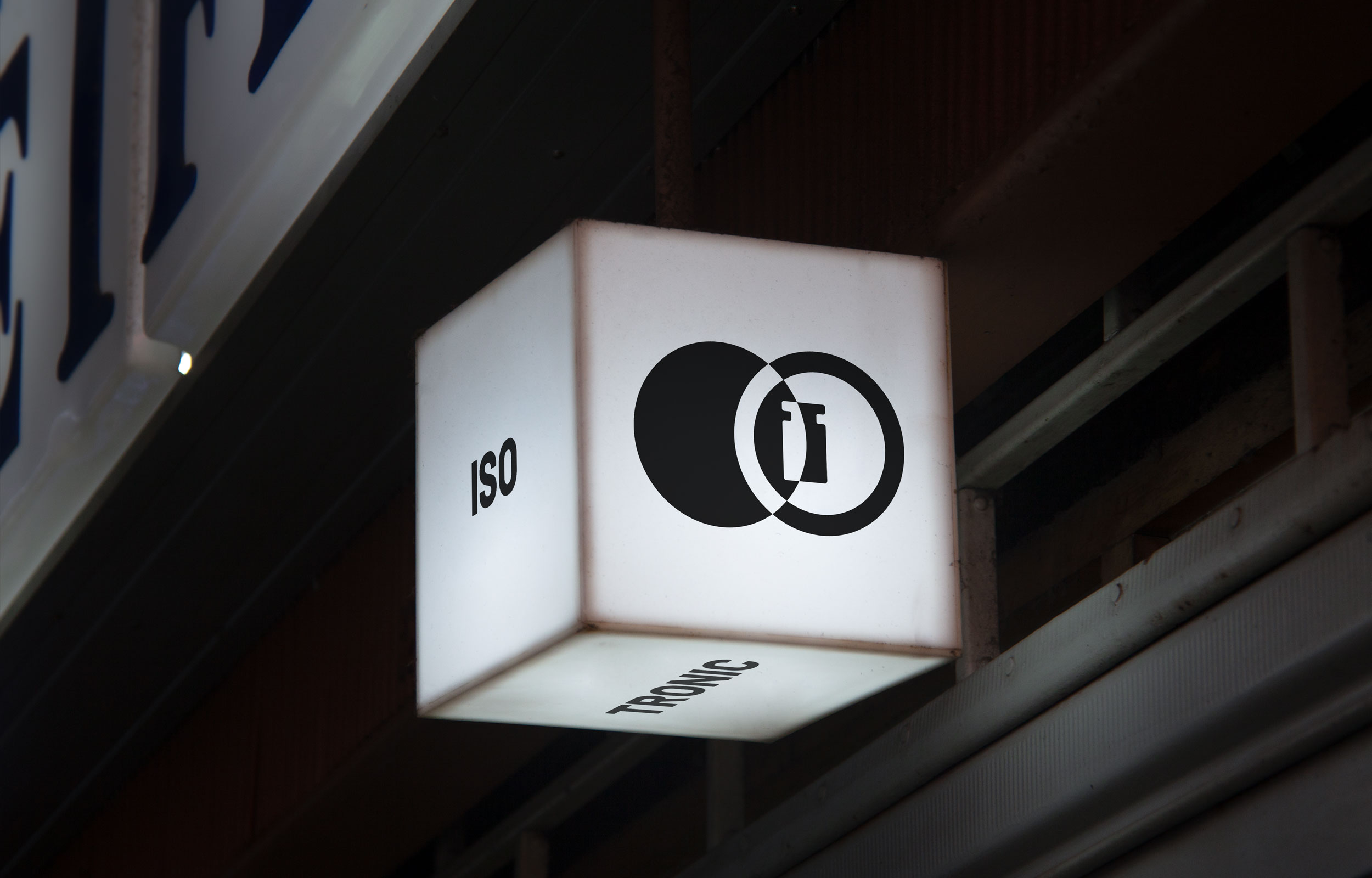 Illuminated square Isotronic sign with black circular logo at night