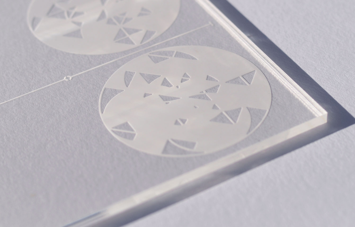 Close-up of circular triangular-fragment engravings on a clear acrylic panel