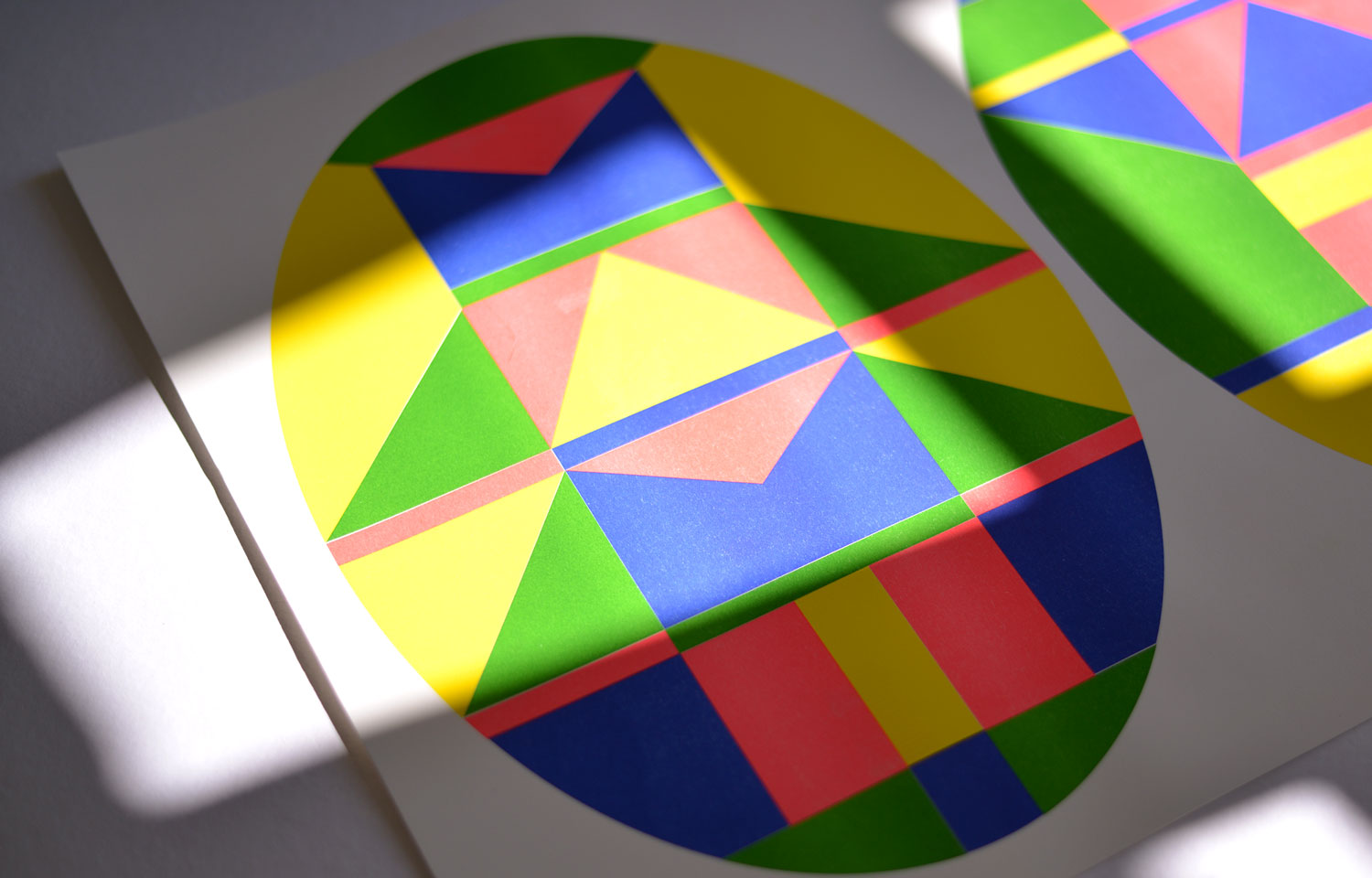 Close view of overlapping printed oval geometric artworks crossed by bright sunlight and shadows
