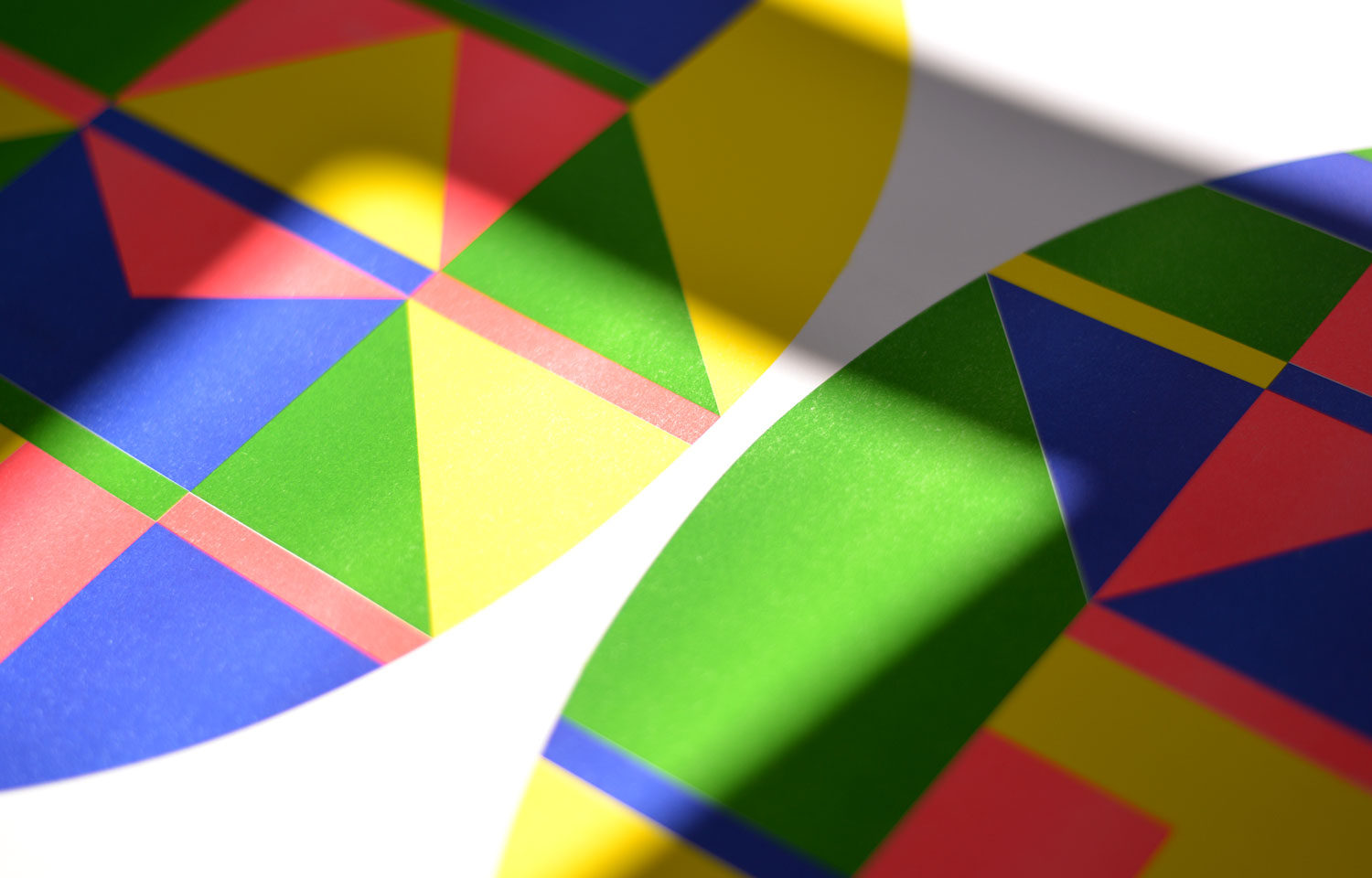Detail of layered geometric colour fields on oval prints, partly covered by diagonal shadows