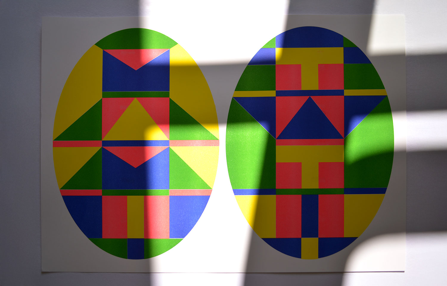 Two colourful oval geometric prints displayed side by side, with sunlight falling across them