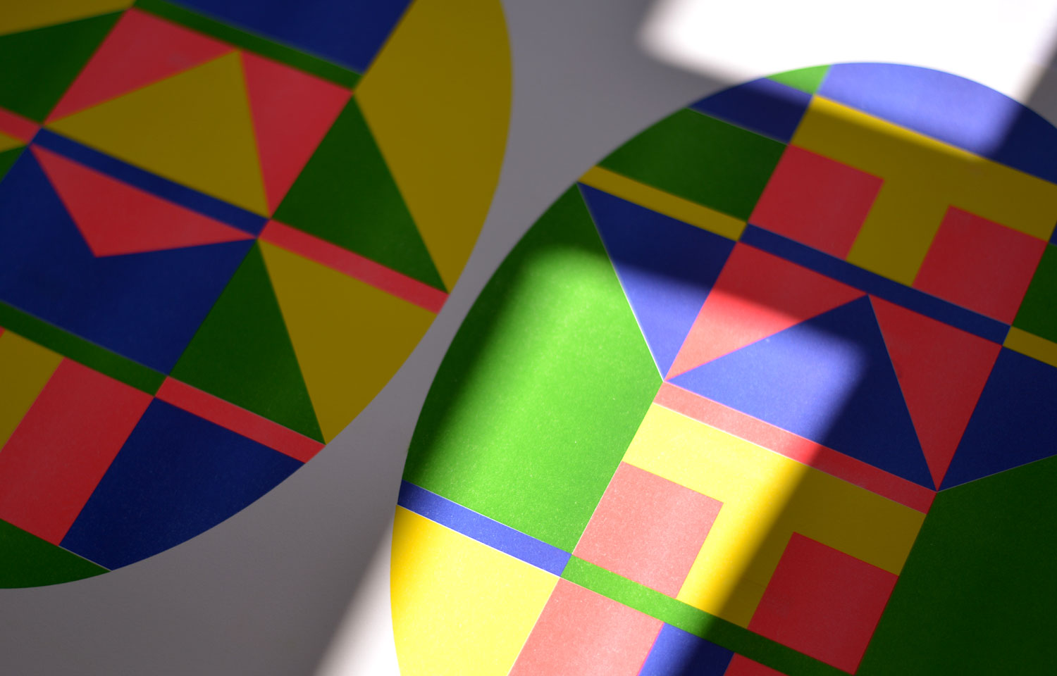 Sunlit close-up of two colourful oval geometric prints with angular red, blue, green and yellow shapes