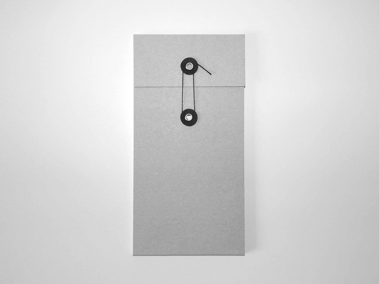 Tall grey folded paper object with a small black circular fastening