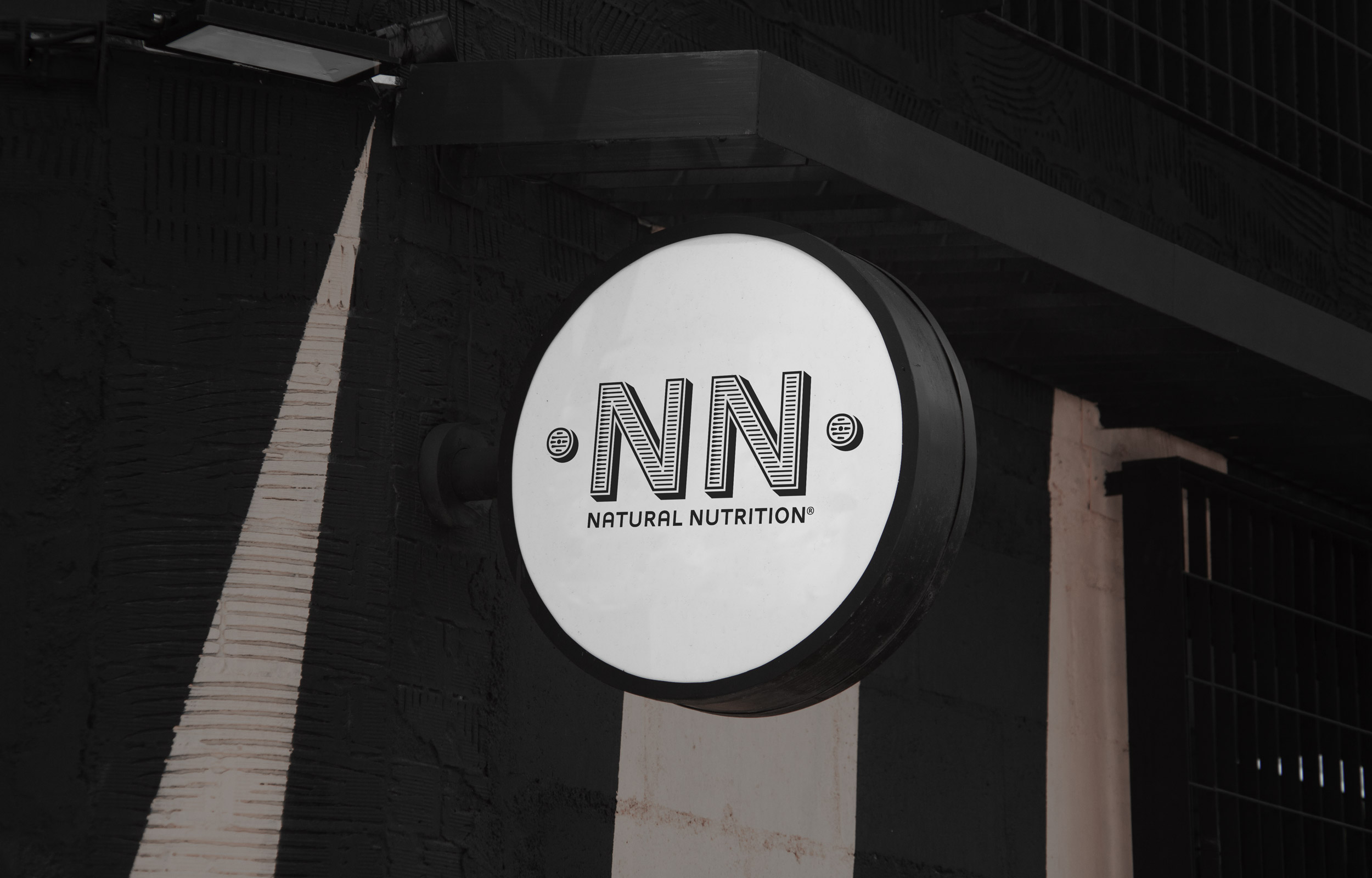 Round illuminated NN Natural Nutrition sign on a dark building facade