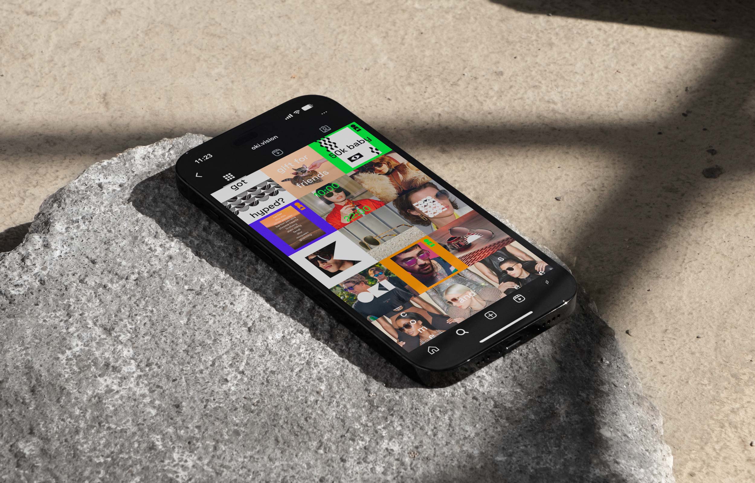 Smartphone displaying a grid of colourful Oki social media images on a stone surface