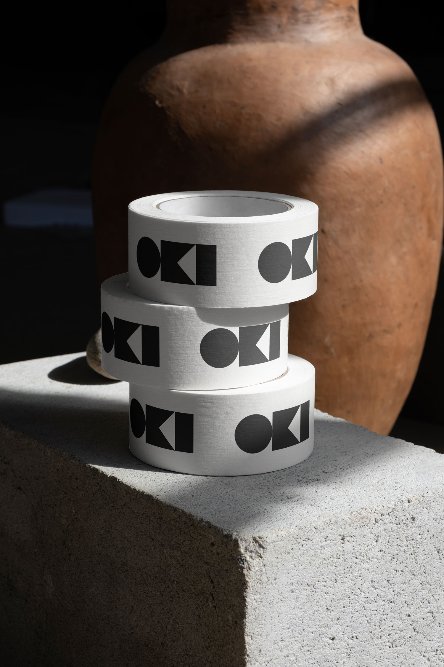 Rolls of white tape printed with black Oki symbols stacked on a concrete block