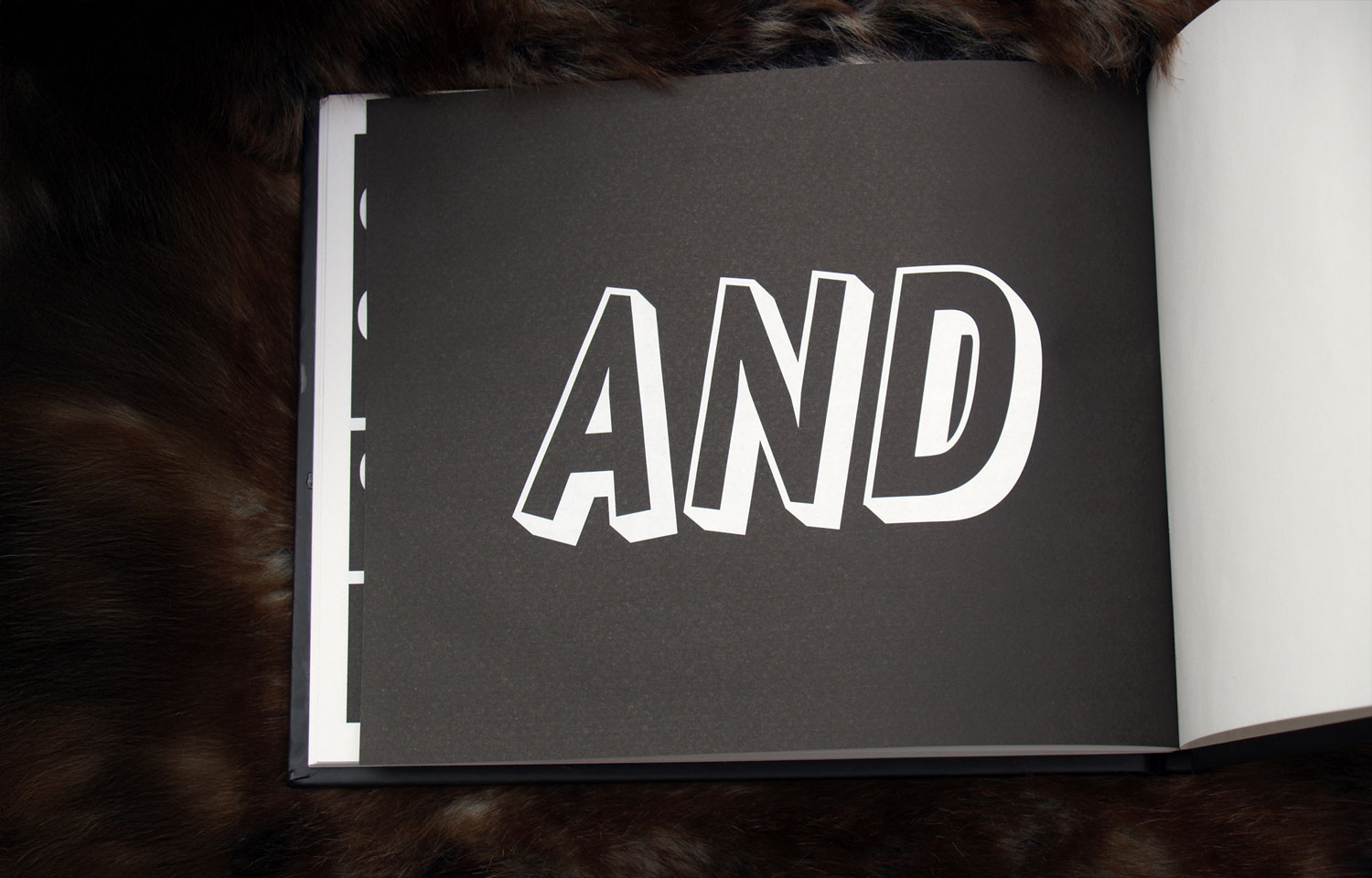 Open book spread with the word AND in large white outlined letters on black