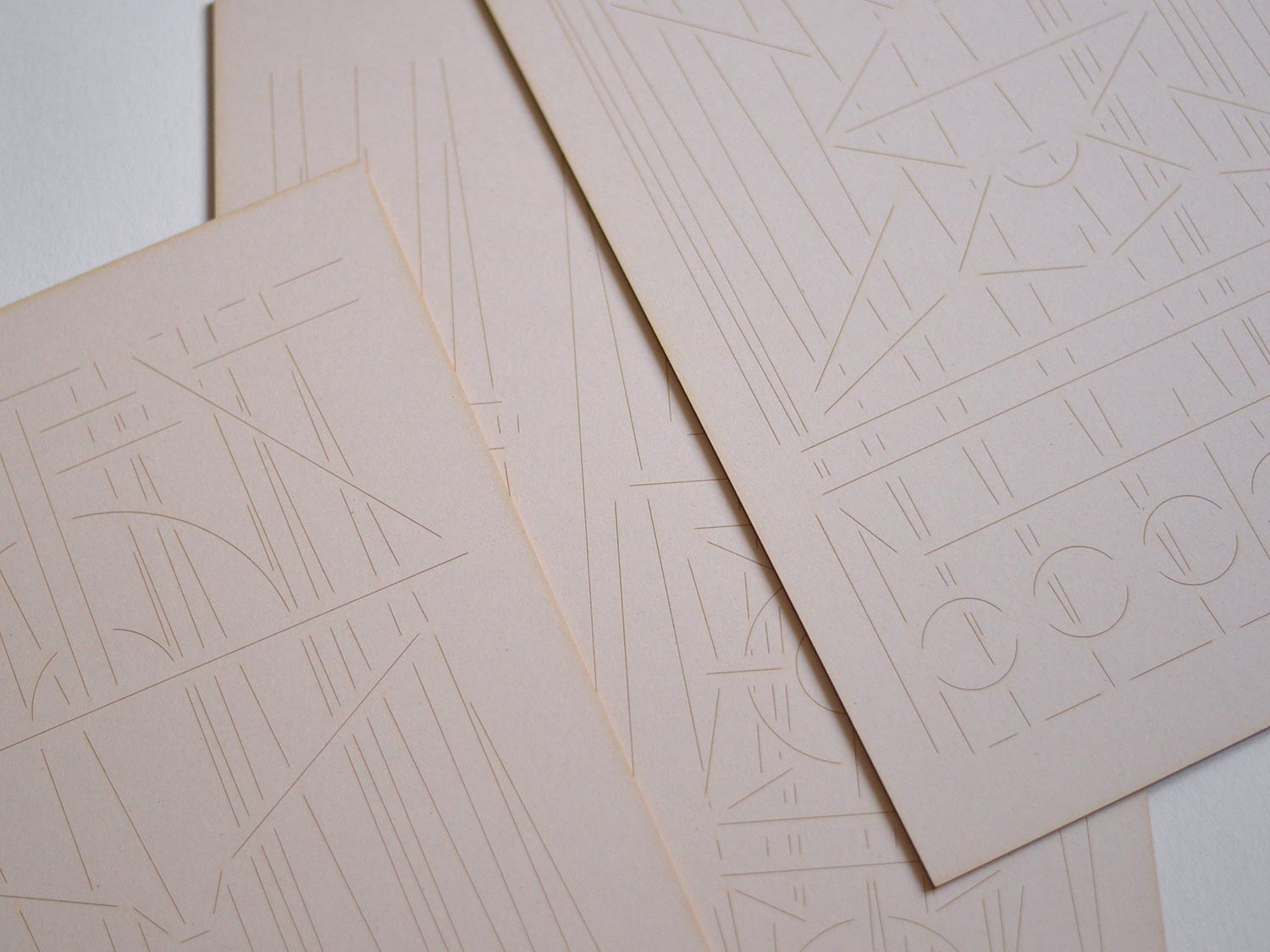 Two overlapping pale cards embossed with fine geometric line designs