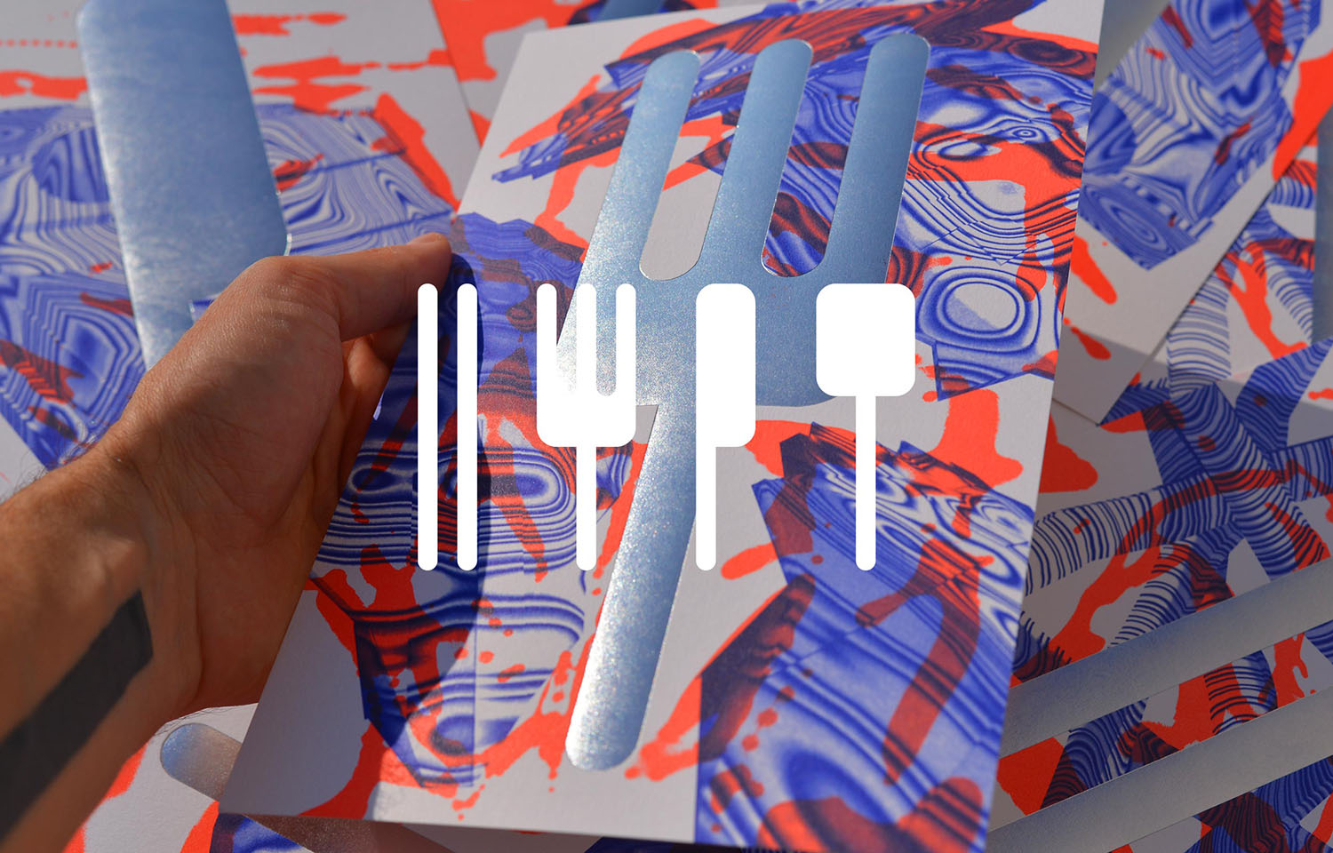 Hand holding colourful printed artwork with a white cutlery motif