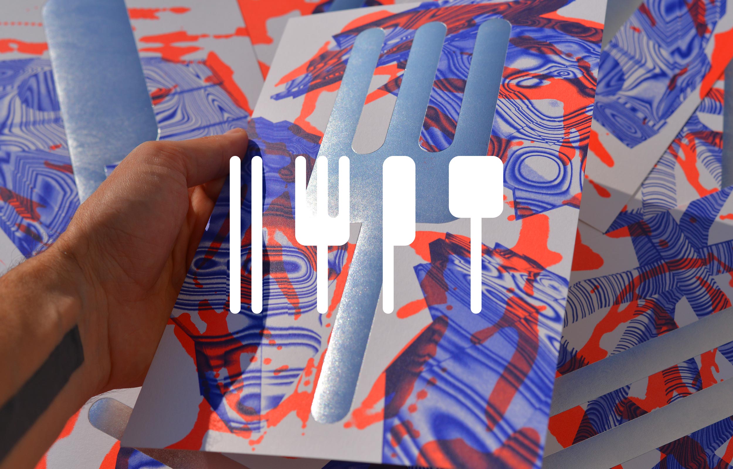 Hand holding a silver fork-shaped metal object over a red and blue marbled print