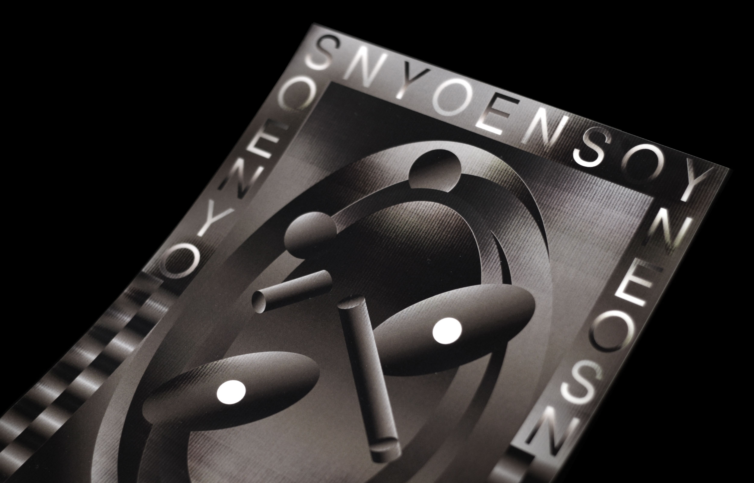 Angled close-up of a black-and-silver poster with looping forms and lettered border